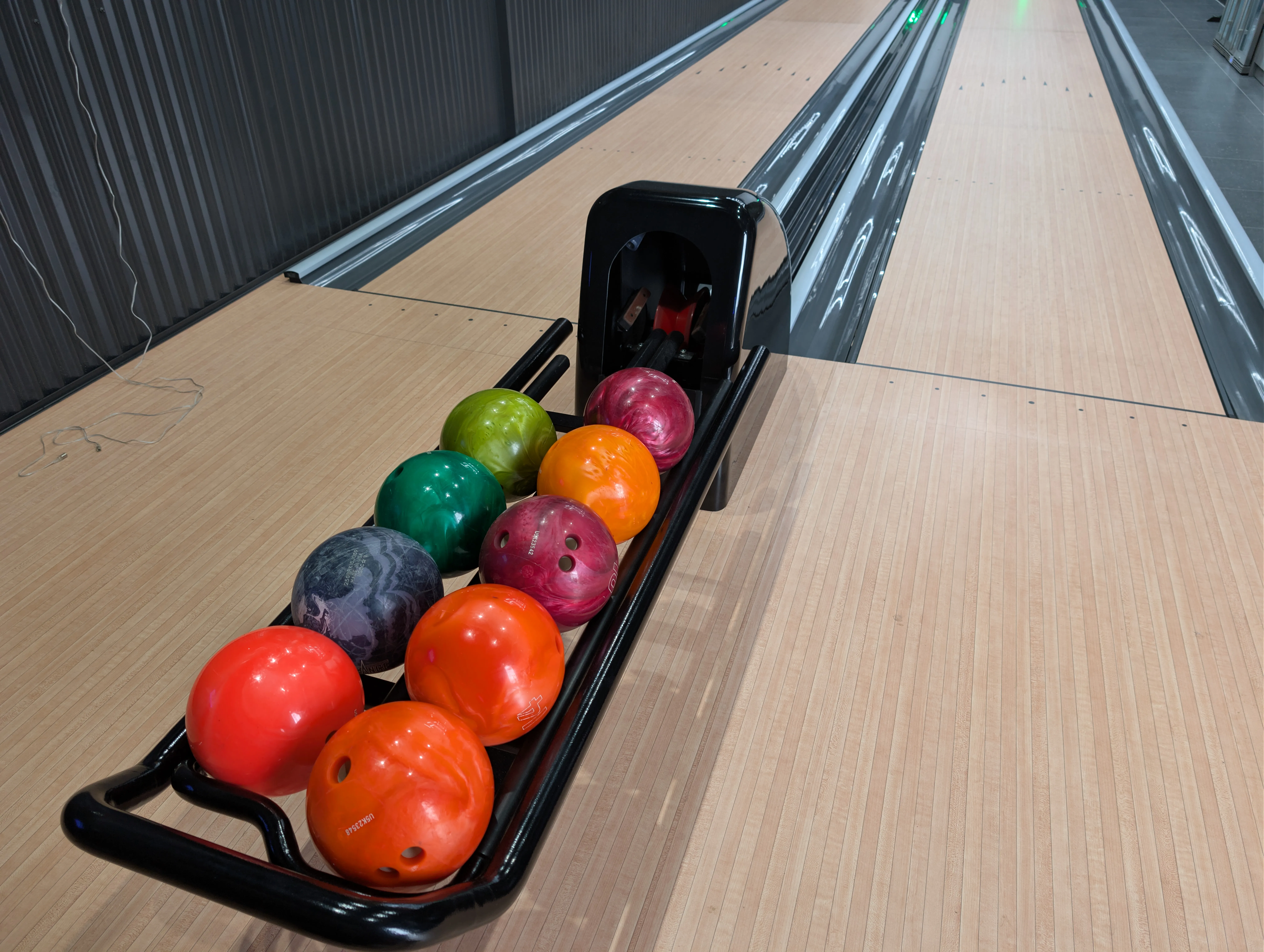 Colourful bowling balls on a black ball return between two private bowling lanes