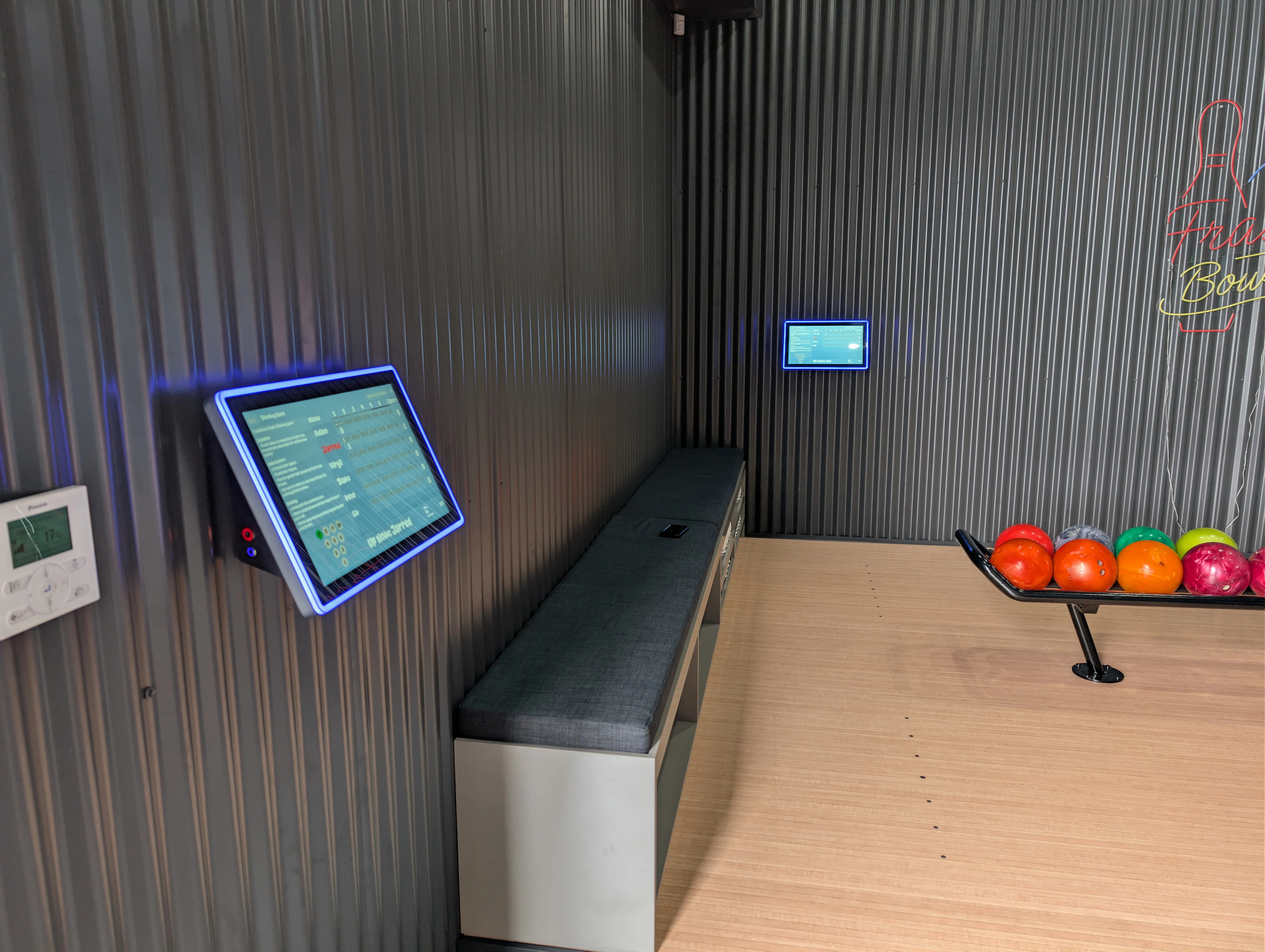Two touchscreen scoring consoles mounted on the side wall beside the bench seating