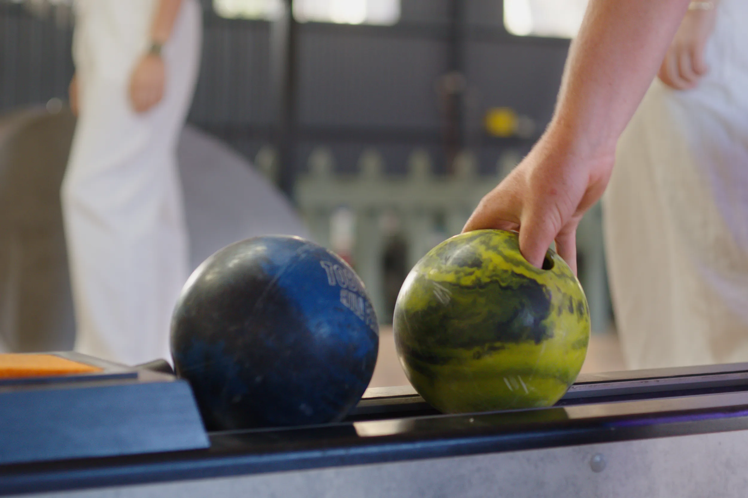 Hand reaching for a marbled bowling ball with people in the background